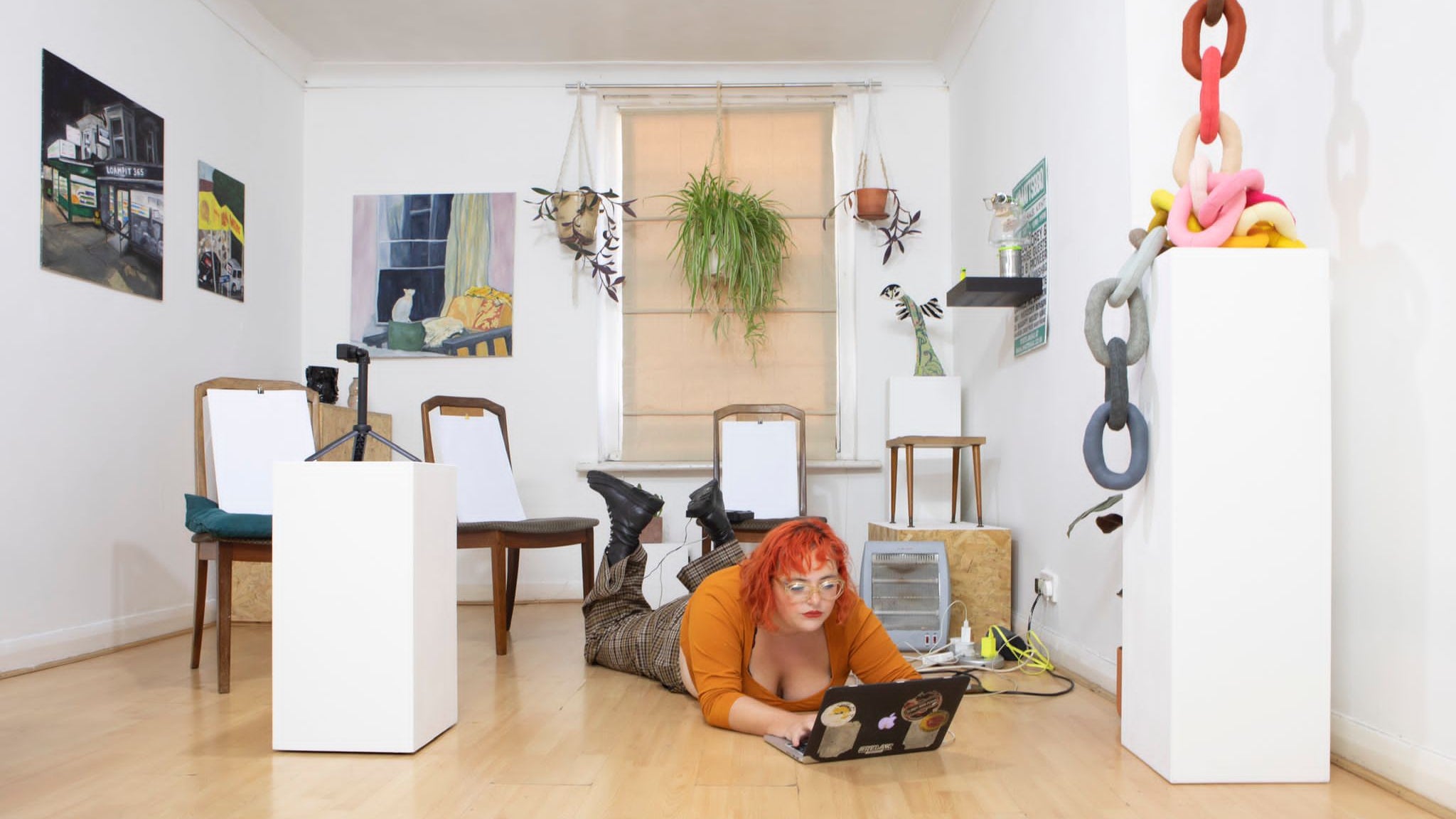 The Artist Lily Holder lying on the floor in a gallery space surrounded by Artworks and drawing boards set up for a Life Drawing class.